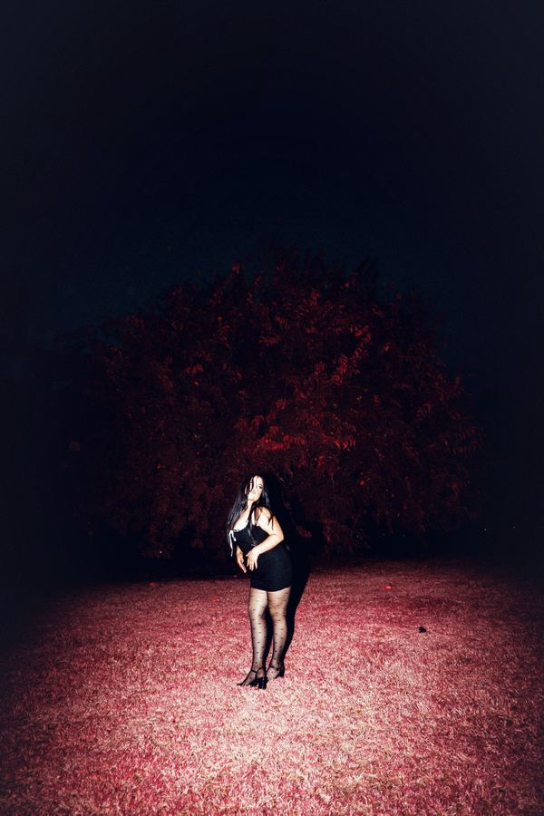 A figure in flash on red-lit grass beneath a dark tree